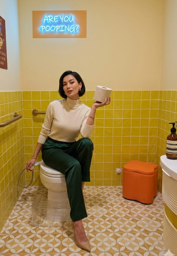 Person sitting on a toilet in a bathroom with a neon sign and colorful decor.